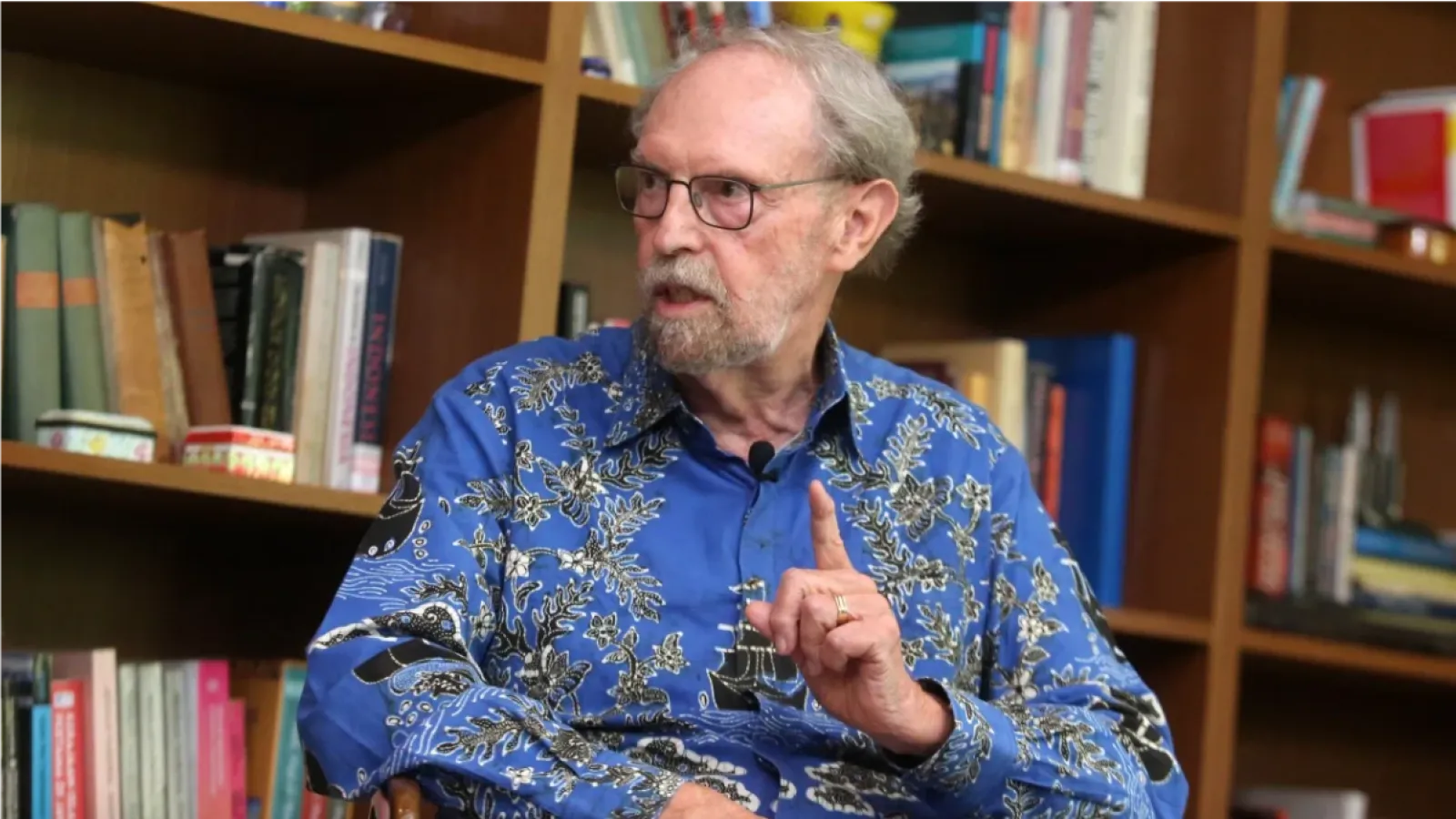 William Liddle, a white older man in a blue shirt talking in front of a bookcase