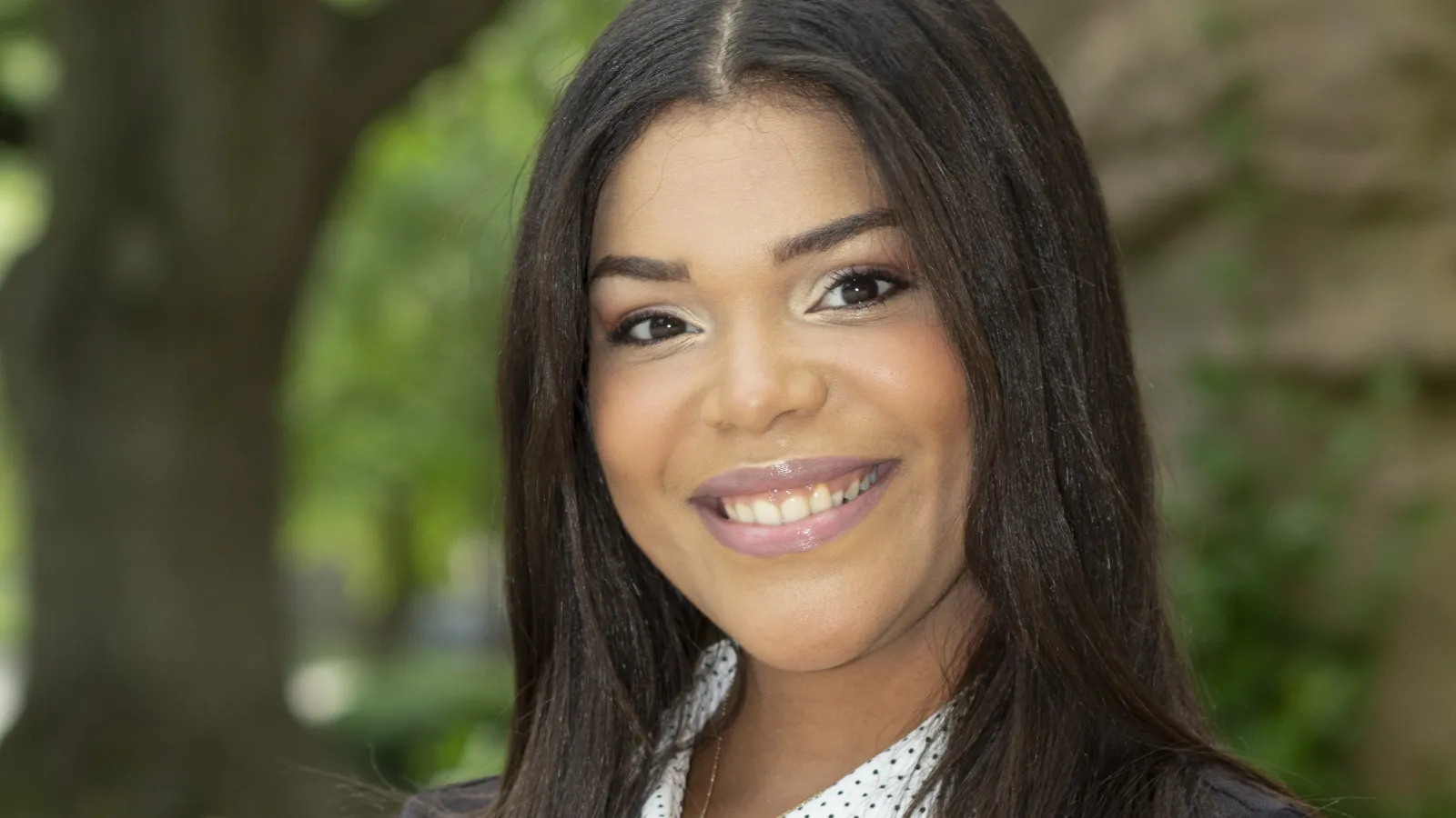 Franshelly headshot, wearing black shirt with white collar, arms crossed, smiling at camera