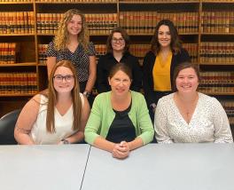 Group of 6 women sitting at a table in front of a bookcase