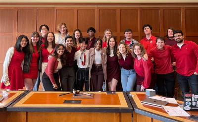 Model UN team posing behind a wooden table with red and white shirts on